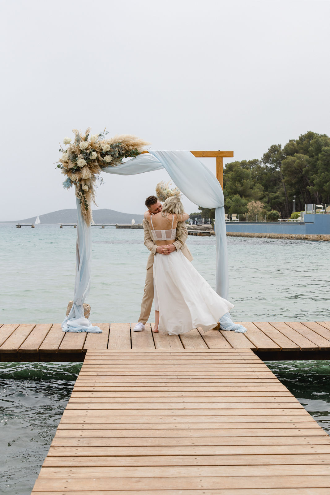 Bild von einem Hochzeitspaar das sich auf einen Steg umarmt.