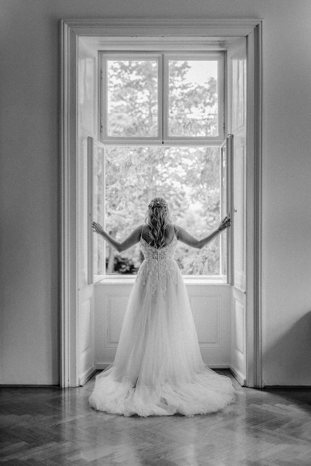 Schwarz weiß Bild von einer Braut die vor einen offenen Fenster steht.