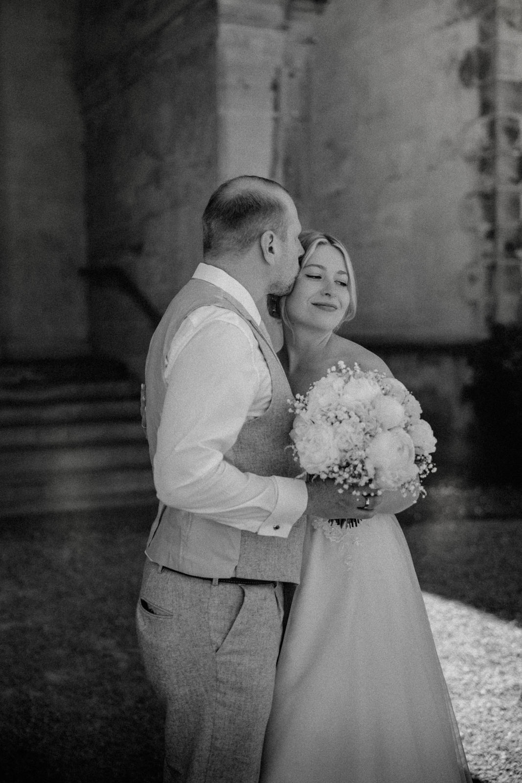 Bild in schwarz weiß von einen Ehepaar, auf dem Der Bräutigam der Braut einen Kuss auf die schläge gibt.